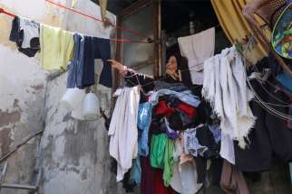 A woman removes dry clothes from her home in a poor section of Tripoli, Lebanon, July 1, 2020. Lebanese have seen their national currency lose 80% of its value against the U.S. dollar, a majority currency also used in the country, since nationwide protests erupted in October.