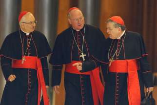 Cardinals Mauro Piacenza, prefect of the Congregation for Clergy, Timothy M. Dolan of New York, and Raymond L. Burke, prefect of the Supreme Court of the Apostolic Signature, talk as they walk through Paul VI hall before the morning session of the extrao rdinary Synod of Bishops on the family at the Vatican Oct. 16.