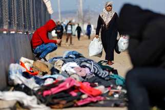 A refugee woman from Syria carries food while other displaced people sit near a border gate in Kilis, Turkey, Feb. 9. More than 30,000 people are stranded in northern Aleppo province after Turkish government forces closed border crossings.