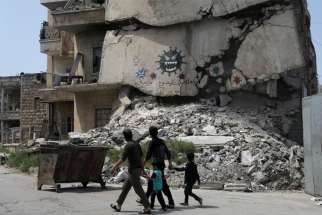 People walk past a damaged building depicting drawings alluding to COVID-19 encouraging people to stay at home in Idlib, Syria April, 18, 2020. Religious freedom advocates and health care professionals have expressed concerns about the COVID-19 response in northeast Syria.