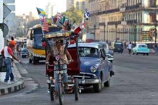 A man rides a bicycle taxi with several national flags on it along a street in late March in Havana. Pope Francis will visit Cuba in September before his trip to the United States.