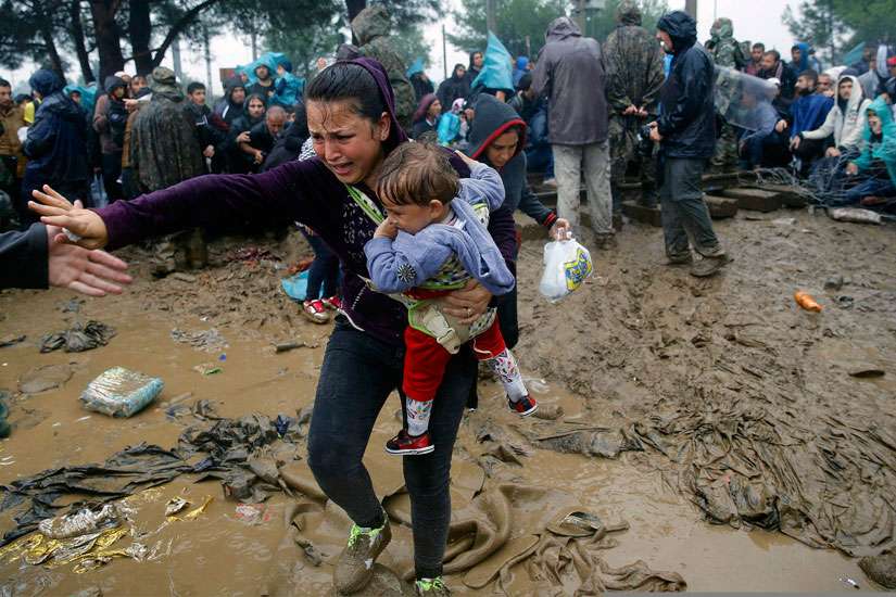 A Syrian refugee woman cries as she carries her baby through the mud to cross the border from Greece into Macedonia near the Greek village of Idomeni Sept. 10.