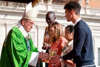 Pope Francis accepts offertory gifts during the opening Mass of the Synod of Bishops on young people, the faith and vocational discernment in St. Peter&#039;s Square at the Vatican Oct 3. Among those presenting the gifts was Emilie Callan, a synod delegate from Canada, pictured with the young adults second from left.