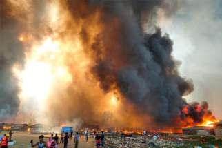 People stand amid smoke and flames after a fire broke out at a Rohingya refugee camp in Cox&#039;s Bazar, Bangladesh, March 22, 2021. The fire swept through the camp, killing at least five people, destroying homes and endangering the lives of tens of thousands of refugees, camp officials said.