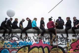 People sit on the East Side Gallery and watch a circus performance in Berlin Nov. 9. The president of the German bishops&#039; conference praised Catholics who helped bring down the Berlin Wall, but also urged the church to look ahead to its future mission.
