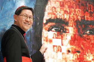 Philippine Cardinal Luis Antonio Tagle, president of Caritas Internationalis, points to a photo of his maternal grandfather on a mosaic created for the 2019 general assembly of Caritas Internationalis. Tagle said Caritas must push a “politics of communion.”