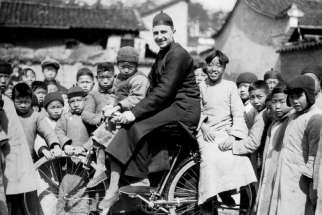 Fr. Craig Strang on his bicycle is given plenty of attention from his pupils in the 1930s.