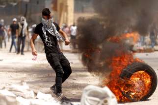  A Palestinian protester in Beita, West Bank, moves a burning tire during clashes with Israeli troops April 28. Catholic leaders in the Holy Land urged Israel to concede to demands of Palestinian political prisoners on a hunger strike since April 17.