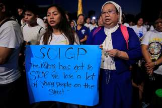 A young woman displays a placard as a nun prays the rosary Feb. 24 during a protest against plans to reimpose the death penalty and intensify the drug war during a &quot;Walk for Life&quot; rally at a park in Manila, Philippines.