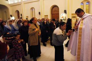 A priest gives Communion during Mass at a church in Baghdad March 1. Christian organizations have begun funneling aid to Syrian cities that are housing refugees from the Islamic State. 