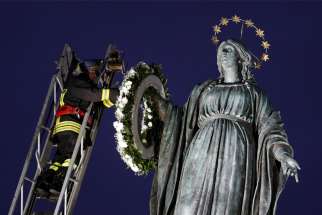 A firefighter places a wreath on a tall Marian statue overlooking the Spanish Steps in Rome Dec. 8, 2021, the feast of the Immaculate Conception. Pope Francis prayed at the statue before daybreak, continuing the papal tradition of visiting the Spanish Steps on the feast of the Immaculate Conception.