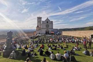People sit outside the Basilica of St. Francis in Assisi as they attend the beatification Mass of Carlo Acutis in Assisi, Italy, Oct. 10, 2020. The Mass was held inside the basilica but measures to prevent the spread of COVID-19 meant that most of the attendees sat outside. 