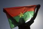 A protester holds up a Burkina Faso flag in Ouagadougou, the capital of Burkina Faso, in 2014. At least 15 people were killed in an attack by gunmen on Catholics gathered for Sunday Mass in a Burkina Faso village Feb. 25, 2024.