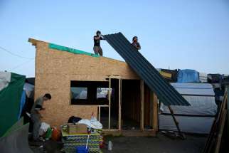 Men remove the roofing of a makeshift shelter Oct. 25, as part of the dismantlement of the camp called the &quot;Jungle&quot; in Calais, France.