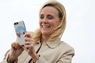 A woman with a smartphone cover featuring Pope Francis takes pictures as people await his on the airfield at Joint Base Andrews in Maryland Sept. 22, 2015.