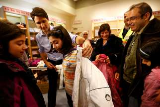 Prime Minister Justin Trudeau helps a young Syrian refugee try on a winter coat after she and her family arrived in Toronto from Beirut in December 2015. 