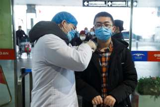 A medical official takes the body temperature of a man Jan. 27, 2020, at the departure hall of the airport in Changsha, China, as the country is hit by an outbreak of a new coronavirus. The virus has spread to almost every province in mainland China during Lunar New Year.