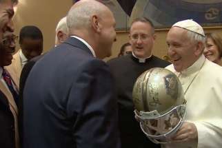 Pope Francis jokes with an NFL Hall of Fame representative about wearing a helmet that was a gift for the Pope during a visit at the Vatican on June 21, 2017. 