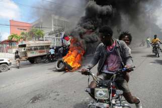 People drive past a burning blockade as demonstrators hold a protest calling for the resignation of Haitian Prime Minister Ariel Henry outside the Canadian Embassy in Port-au-Prince Feb. 25 2024.