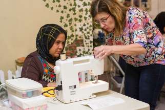  A volunteer works with a refugee from Afghanistan to help her learn how to use a sewing machine during an April 27 training session at a Catholic Charities program in Fredericksburg, Va.