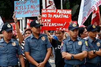  Philippine police keep watch as protesters hold signs against martial law extension in Mindanao Dec. 13. Congress approved a request by President Rodrigo Duterte to extend martial law across the region until Dec. 31, 2018. 
