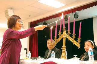 A volunteer lights the candles, as Fr. Dominic Qin watches, to begin the Passover celebrations at Chinese Martyrs parish.