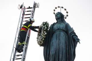 A firefighter places a wreath on a Marian statue overlooking the Spanish Steps in Rome Dec. 8, 2019, the feast of the Immaculate Conception.