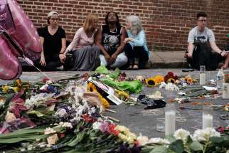 People sit by a memorial of flowers in Charlottesville, Va., Aug. 14 where an Aug. 12 car attack took place against counter-protesters demonstrating at a rally of white nationalists.