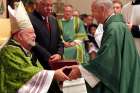 Bishop Daniel R. Jenky of Peoria, Ill., hands a copy of the &quot;positio&quot; on Archbishop Fulton J. Sheen&#039;s life to Father James O&#039;Brien, representing the late Cardinal Francis E. George and the Archdiocese of Chicago, during a Mass at the Cathedral of St. Mary of the Immaculate Conception in Peoria Sept. 9, 2012. Supporters of the canonization cause for Archbishop Sheen are invited to participate in a nine-day novena starting Dec. 12, 2019, to &quot;petition God unceasingly to remove all obstacles&quot; for the beatification of the media pioneer, author and evangelist. Archbishop Sheen&#039;s beatification was scheduled for Dec. 21 but has been postponed.