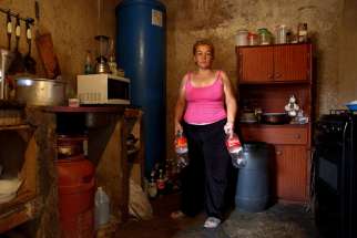 Yunni Perez holds plastic bottles used to carry water while she poses for a photo inside her home in a Caracas slum.