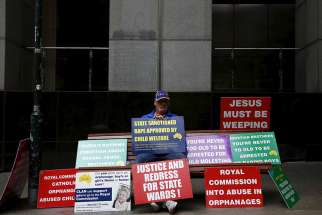 Abuse victim Darren Chalmers sits on a bench with numerous placards outside the venue for Australia&#039;s Royal Commission Into Institutional Responses to Child Sexual Abuse in Sydney March 2016.