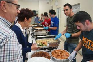 Husam Al Dakhil and his cousin Bahaa Hraiz serve a Syrian buffet. The cousins came to Canada a little more than a year ago. Now Holy Redeemer parish has found sponsors for their parents and siblings.