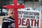 A woman holds a sign and cross as members of the local Chaldean community demonstrate June 16 outside the Patrick V. McNamara Federal Building to protest the arrest and detention of more than 100 Chaldean Christians from the Detroit area.