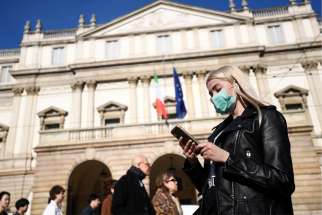 A woman wearing a face mask checks her phone outside the Teatro alla Scala opera house, closed by authorities due to a coronavirus outbreak in Milan Feb. 24, 2020. The Archdiocese of Milan issued a notice Feb. 23 suspending all public celebrations of Mass until further notice in compliance with Italian Ministry of Health precautions to prevent the further spread of the coronavirus.