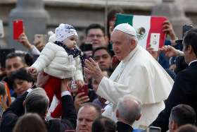 A guard lifts a baby for Pope Francis to greet as the pope leads his general audience in St. Peter&#039;s Square at the Vatican Nov. 6, 2019.