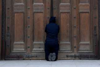 A person prays at the closed doors of London&#039;s Westminster Cathedral on Easter, April 12, 2020, during the COVID-19 pandemic. Churches in England and Wales must wait until July before they may reopen under a coronavirus recovery strategy published by the government.