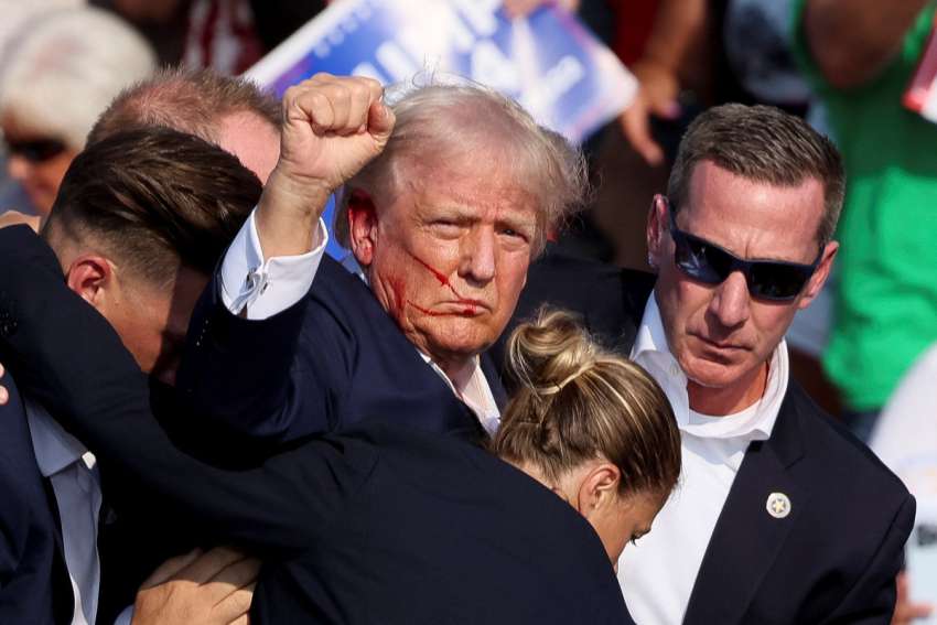 Republican presidential candidate and former U.S. President Donald Trump gestures, with blood on his face, is assisted by guards after shots were fired during a campaign rally at the Butler Farm Show in Butler, Pa., July 13, 2024. A local prosecutor says the suspected gunman and at least one attendee are dead.