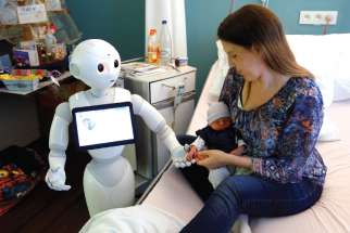 “Pepper,” a humanoid robot designed to welcome and take care of visitors and patients, holds the hand of a newborn baby next to his mother at AZ Damiaan hospital in Ostend, Belgium. The Vatican’s Pontifical Academy for Life has added robotics to its list of specialized areas of study. 