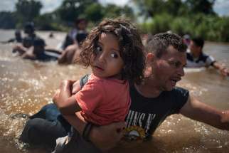 A man, part of a caravan of migrants from Central America to the United States, carries a girl Oct. 29 through the Suchiate River into Mexico from Guatemala. 