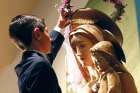 Second-grader climbs a ladder to place a wreath of flowers atop a statue of Mary and the Christ Child.