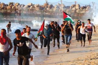 Palestinians run for cover from tear gas fired by Israeli troops during a protest along a beach in the Gaza Strip.