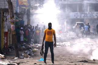 A man holds a weapon next to burning barricades during anti-government protests Feb. 17 in Port-au-Prince, Haiti. 
