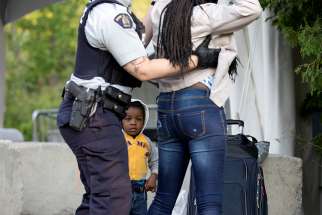 Two-year-old Evanston, whose family stated they are from Haiti, watches as a Royal Canadian Mounted Police officer pats down his mother before the two cross the U.S.-Canada into Quebec Aug. 29, 2018. 