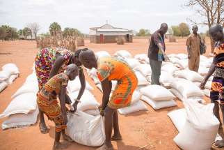 Young women help each other carry sacks of sorghum and beans March 17 after receiving them at a distribution center in Yirol, South Sudan. July 9 marks the sixth anniversary of worldÕs youngest country as it is 